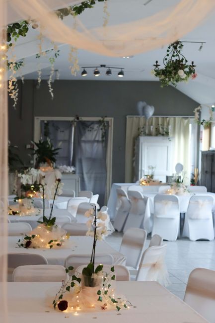 A beautifully decorated indoor venue featuring soft pastel-colored floral arrangements and elegant table settings for a wedding celebration. Each table is adorned with white tablecloths, fairy lights,